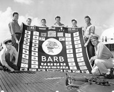 Crew members of the USS Barb pose with the battle flag at Pearl Harbor. At the bottom of the flag, you can see the train symbol.